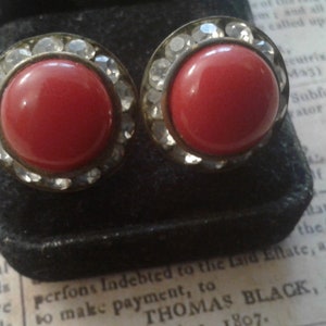 May include: A pair of red and silver earrings with a round red stone surrounded by clear rhinestones.
