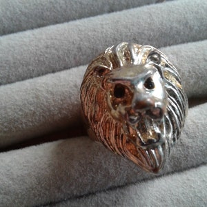 May include: A silver and gold lion head ring. The lion's mane is detailed and the eyes are black.
