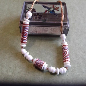 Può includere: Una collana con perline cilindriche bianche e rosse con un motivo a spirale. Le perline sono infilate su una catena dorata.