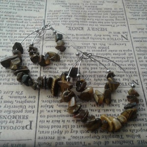 May include: A pair of gold and brown tiger's eye stone earrings. The earrings are made with small, irregular shaped stones strung on a silver wire hoop.