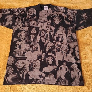 K&ouml;nnte beinhalten: Schwarzes T-Shirt mit einer Collage von Marilyn Monroe-Bildern in Grau- und Wei&szlig;t&ouml;nen. Das Design zeigt verschiedene Posen der Schauspielerin. Das T-Shirt hat kurze &Auml;rmel und einen Rundhalsausschnitt.
