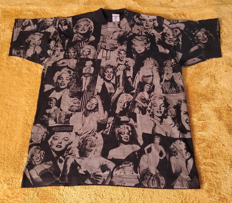 K&ouml;nnte beinhalten: Schwarzes T-Shirt mit einer Collage von Marilyn Monroe-Bildern in Grau- und Wei&szlig;t&ouml;nen. Das Design zeigt verschiedene Posen der Schauspielerin. Das T-Shirt hat kurze &Auml;rmel und einen Rundhalsausschnitt.