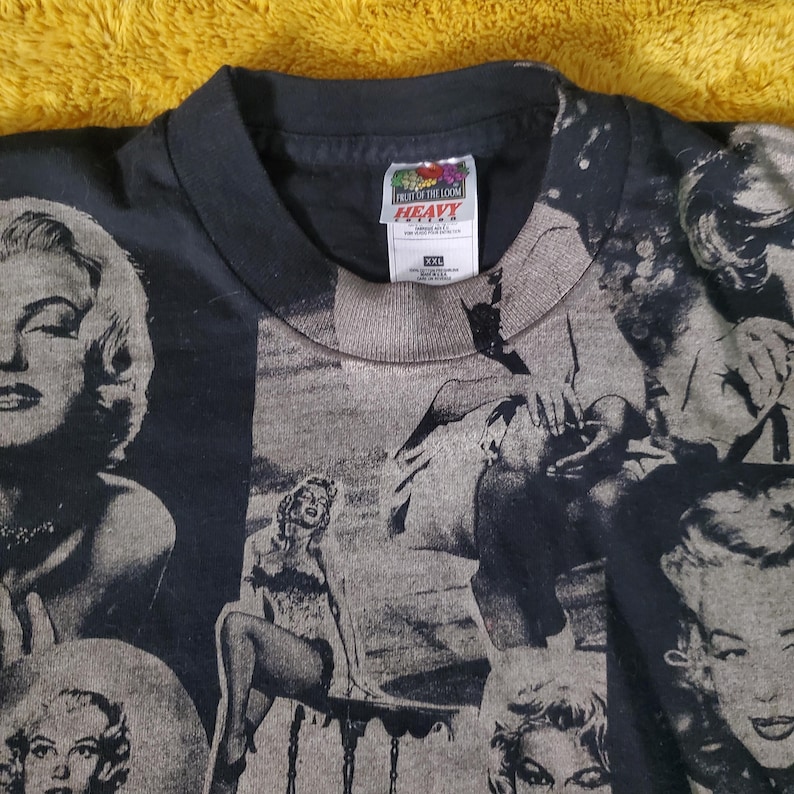 K&ouml;nnte beinhalten: Schwarzes XXL-T-Shirt mit einer Collage von Marilyn Monroe-Bildern in Graustufen. Das Shirt hat einen Rundhalsausschnitt und kurze &Auml;rmel. Das Etikett lautet "FRUIT OF THE LOOM HEAVY".