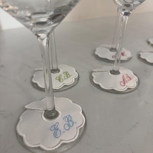 Peut inclure: Verres &agrave; martini transparents avec des marque-verres blancs festonn&eacute;s personnalis&eacute;s. Chaque marque-verre porte des initiales brod&eacute;es en diff&eacute;rentes couleurs, dont le bleu, le vert et le rose. Les marque-verres sont con&ccedil;us pour s'adapter &agrave; la tige du verre.