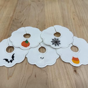 Peut inclure: Ensemble de dessous de verre blancs à bord festonné avec des motifs brodés sur le thème d'Halloween. Chaque dessous de verre présente un motif différent : une citrouille, une toile d'araignée, une chauve-souris, un fantôme et des bonbons.
