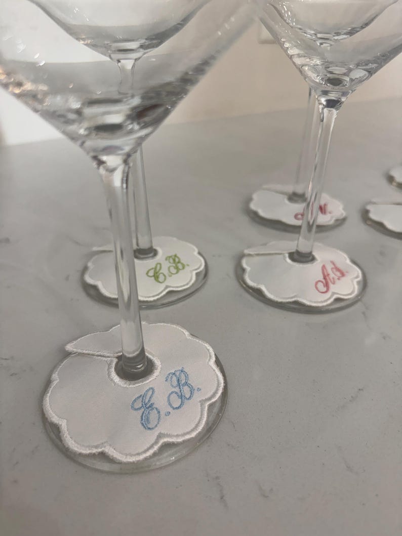 Peut inclure: Verres &agrave; martini transparents avec des marque-verres blancs festonn&eacute;s personnalis&eacute;s. Chaque marque-verre porte des initiales brod&eacute;es en diff&eacute;rentes couleurs, dont le bleu, le vert et le rose. Les marque-verres sont con&ccedil;us pour s'adapter &agrave; la tige du verre.