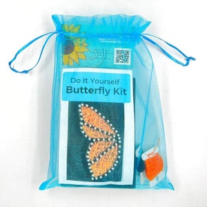 May include: A blue organza bag with a white card that says "Do It Yourself Butterfly Kit". The card has a picture of a butterfly made with orange thread on a black background. The bag also contains a small spool of orange thread.