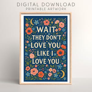 May include: Framed art print with a navy blue background and floral design. The artwork features the text "WAIT THEY DON'T LOVE YOU LIKE I LOVE YOU" in cream lettering. Floral elements include orange, pink, and blue flowers, with crescent moons and stars.