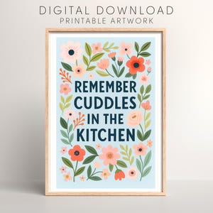 Può includere: Una stampa incorniciata con sfondo azzurro, con la scritta "REMEMBER CUDDLES IN THE KITCHEN" in blu navy. L'opera è circondata da illustrazioni floreali nei toni del rosa, pesca e rosso, con foglie verdi. La parte superiore della stampa recita "DOWNLOAD DIGITALE OPERA D'ARTE STAMPABILE."