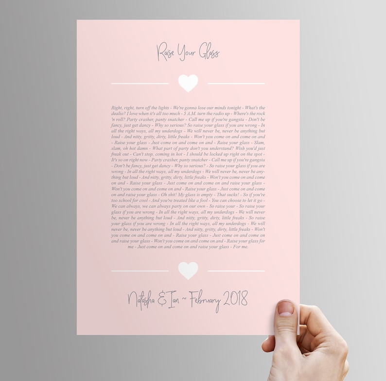 May include: A pink printable wedding sign with a gray heart and text that reads "Raise Your Glass" and includes a song lyric about raising a glass. The text also includes the names "Natasha & Ion" and the date "February 2018".