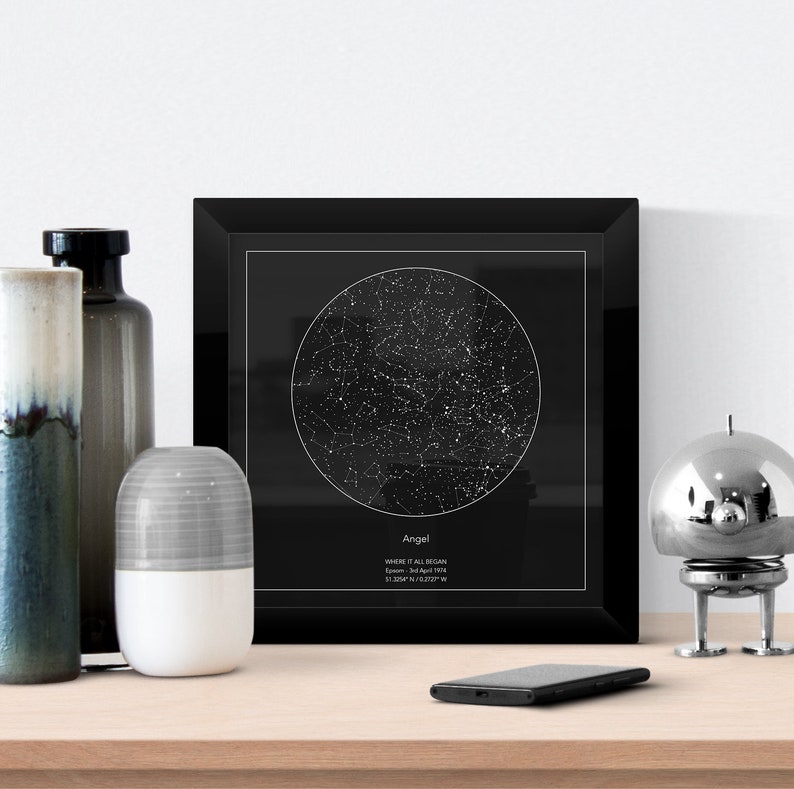 May include: Black framed print with a white circle showing the night sky with stars. The text "Angel" is at the bottom of the print with the text "Where it all began" and the date "London, 14 April 1994" and coordinates "51.5047&deg; N 0.1278&deg; W".