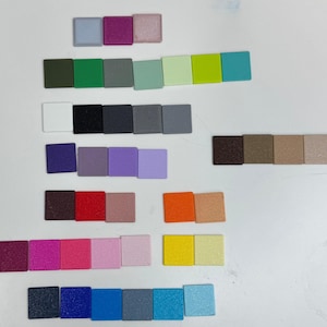 Op de afbeelding: Een verzameling kleine, vierkante tegels gerangschikt in rijen, met een grote verscheidenheid aan effen kleuren, waaronder tinten blauw, groen, rood, geel, paars, roze, oranje, bruin, zwart, wit en grijs met een matte of licht getextureerde afwerking.