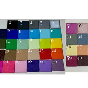 Op de afbeelding: Een verzameling van eenenveertig vierkante kleurstaaltjes gerangschikt in een raster, elk gelabeld met een wit nummer van 1 tot 41. De staaltjes tonen een grote verscheidenheid aan effen, metallic en glitterafwerkingen in kleuren zoals wit, zwart, blauw, groen, geel, rood, oranje, paars, roze en grijs.