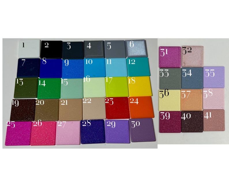Op de afbeelding: Een verzameling van eenenveertig vierkante kleurstaaltjes gerangschikt in een raster, elk gelabeld met een wit nummer van 1 tot 41. De staaltjes tonen een grote verscheidenheid aan effen, metallic en glitterafwerkingen in kleuren zoals wit, zwart, blauw, groen, geel, rood, oranje, paars, roze en grijs.