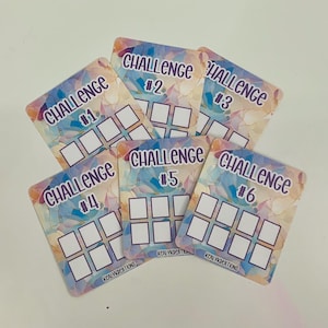 May include: Six colorful challenge cards with the numbers 1 through 6. Each card has a watercolor background and the word "CHALLENGE" printed on it. Each card has six blank squares.