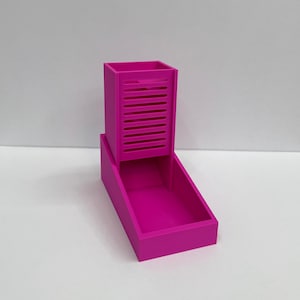 Op de afbeelding: Een felmagenta 3D-geprinte dobbelsteentoren met een verticale rechthoekige kolom met horizontale sleuven aan de voorzijde en een open bak aan de basis om dobbelstenen op te vangen. De structuur is solide, egaal van kleur en glad afgewerkt.