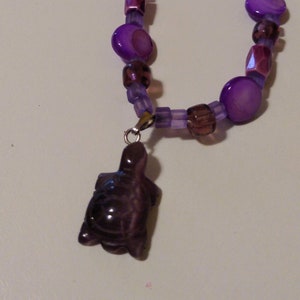 May include: A purple and brown beaded necklace with a purple turtle pendant.