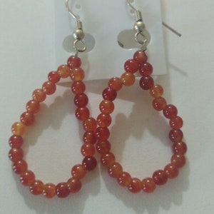 May include: A pair of teardrop-shaped dangle earrings made from orange beads. The earrings are displayed on a white card with the text "New Fashion" printed on it.