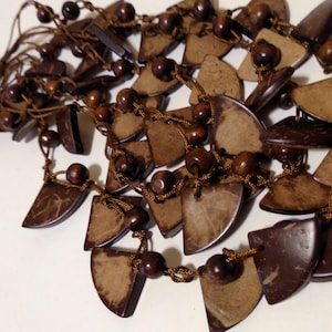 May include: A brown coconut shell necklace with brown wooden beads and a brown cord. The necklace is made of multiple strands of coconut shells and beads.