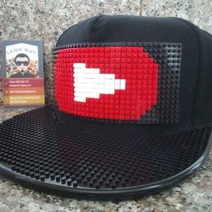 May include: Black baseball cap with a red and white Swiss flag made of Lego bricks on the front. The brim of the cap is also made of Lego bricks.