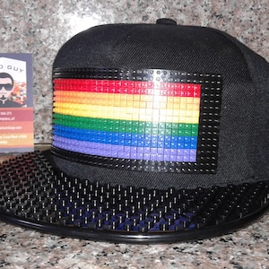 May include: Black baseball cap with a rainbow-coloured Lego brick design on the front. The brim of the cap is also made of Lego bricks.