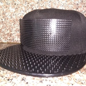 May include: A black baseball cap with a black Lego-style design on the front and brim.