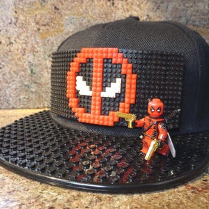 May include: A black and red Lego Deadpool character on a black and red Lego Deadpool themed baseball cap.