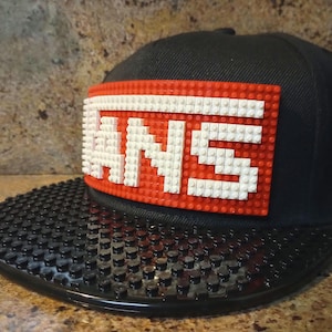 May include: A black and red baseball cap with a white Lego-style "VANS" logo on the front.