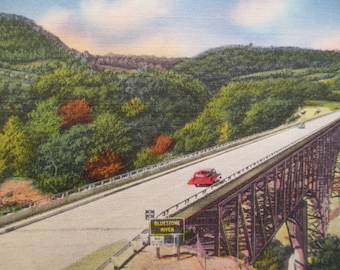 Könnte beinhalten: Eine Vintage-Postkarte, die ein rotes Auto zeigt, das über eine Brücke fährt, auf der ein Schild mit der Aufschrift "Bluestone River" angebracht ist. Die Brücke ist aus Metall und hat ein hölzernes Deck. Das Auto fährt auf einer asphaltierten Straße, die von Bäumen umgeben ist. Die Bäume sind grün und braun, und einige Blätter zeigen Herbstfarben. Der Himmel ist blau und bewölkt.