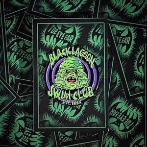 May include: Black and green enamel pin featuring a creature from the Black Lagoon with the text "Black Lagoon Swim Club Est. 1954".