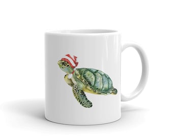 May include: White ceramic mug featuring a green sea turtle wearing a red and white Santa hat. The turtle is swimming to the right.