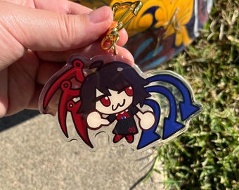 Könnte beinhalten: Ein durchsichtiger Acryl-Schlüsselanhänger mit einer Comicfigur mit schwarzen Haaren, roten Augen und einem rot-blauen Outfit. Die Figur hält eine rot-blaue Waffe. Der Schlüsselanhänger hat einen goldenen Metallverschluss.