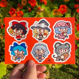 May include: A sheet of six colorful stickers featuring cartoon characters with large eyes. The characters are holding various items, including a loaf of bread, a bottle of milk, and a slice of cheese. The stickers are on a bright orange background.