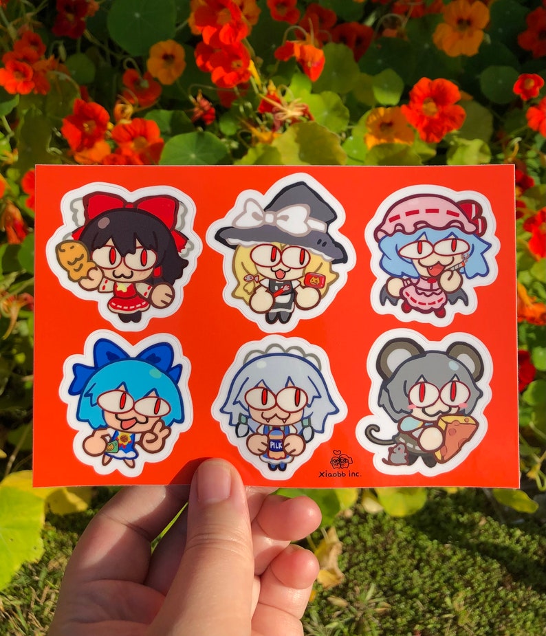 May include: A sheet of six colorful stickers featuring cartoon characters with large eyes. The characters are holding various items, including a loaf of bread, a bottle of milk, and a slice of cheese. The stickers are on a bright orange background.