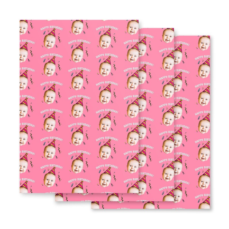 May include: Pink wrapping paper with a repeating pattern of a baby's face wearing a party hat and the text "Happy Birthday!"