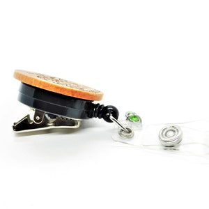 May include: A wooden badge holder with a black clip and a clear retractable badge reel. The reel has two green gem accents.