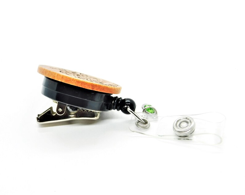 May include: A wooden badge holder with a black clip and a clear retractable badge reel. The reel has two green gem accents.