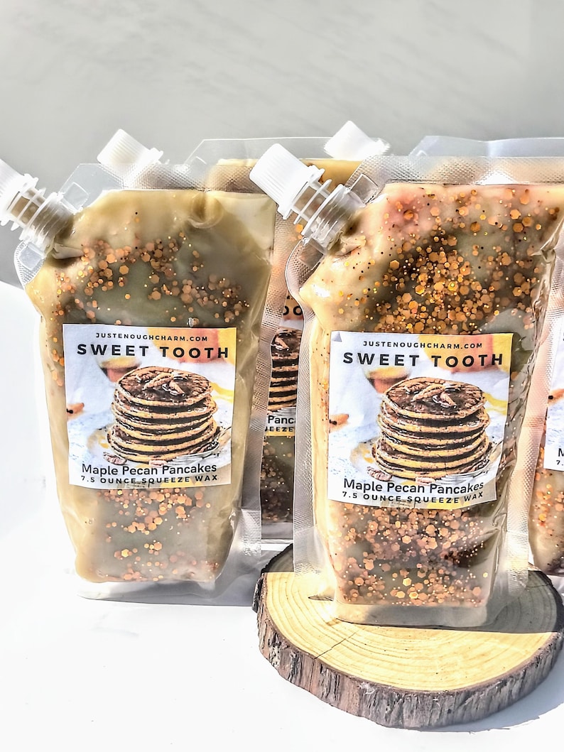 May include: Several clear plastic pouches filled with a light brown wax, speckled with brown and gold granules. Each pouch has a white spout and a label that reads "SWEET TOOTH" and "Maple Pecan Pancakes 7.5 OUNCE SQUEEZE WAX".