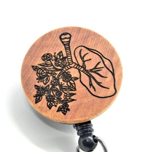 May include: A wooden badge reel with a black and white engraved design of a lung with flowers. The reel is attached to a black retractable cord.