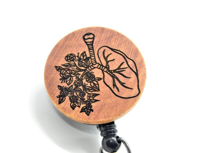 May include: A wooden badge reel with a black and white engraved design of a lung with flowers. The reel is attached to a black retractable cord.