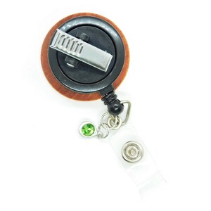May include: A wooden retractable badge reel with a black clip and a green gem. The reel has a clear plastic strap.
