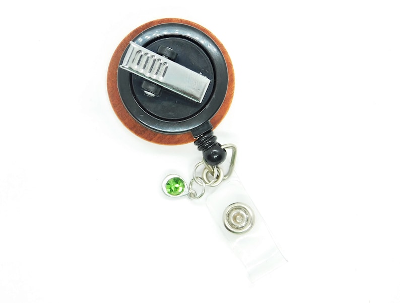 May include: A wooden retractable badge reel with a black clip and a green gem. The reel has a clear plastic strap.
