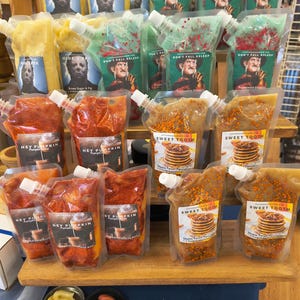 May include: A display of various food pouches with different flavors and labels. The pouches are filled with colorful contents and feature images of horror movie characters. The labels include "Hey Pumpkin," "Sweet Tooth," and "Don't Fall Asleep."