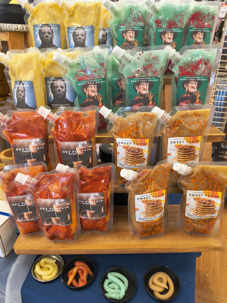 May include: A display of various food pouches with different flavors and labels. The pouches are filled with colorful contents and feature images of horror movie characters. The labels include "Hey Pumpkin," "Sweet Tooth," and "Don't Fall Asleep."