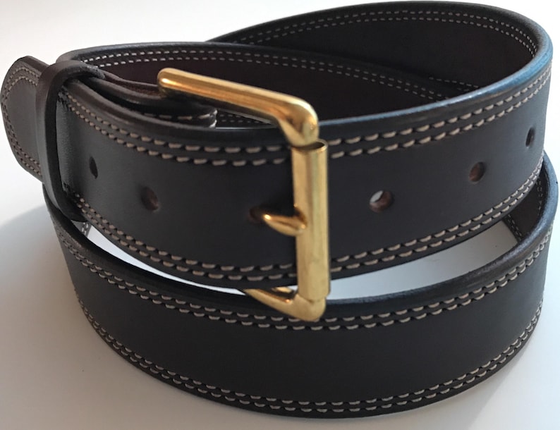 Peut inclure: Une ceinture en cuir marron fonc&eacute; avec une boucle dor&eacute;e et des coutures blanches. La ceinture est pli&eacute;e en deux et la boucle est visible.