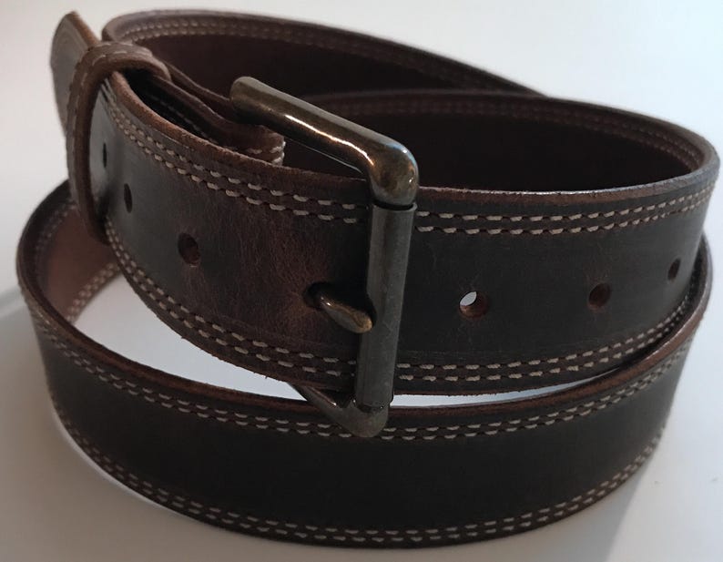 Peut inclure: Une ceinture en cuir marron avec une boucle argent&eacute;e et des coutures blanches. La ceinture est pli&eacute;e en deux et la boucle est visible.