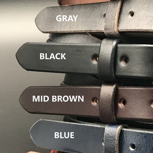 K&ouml;nnte beinhalten: Ein Stapel von sieben Lederg&uuml;rteln in verschiedenen Farben, darunter Kastanie, Used Look, Grau, Schwarz, Mittelbraun, Blau und Rot. Jeder G&uuml;rtel hat ein spitzes Ende und ein einzelnes Loch f&uuml;r eine Schnalle.