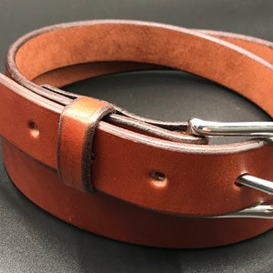 Full Grain Genuine Leather Belt in Chestnut Color with Silver Buckle. The edges are finished and dyed to match the main leather color. The buckle is buckle and the tail place through the keeper. Chicago Screws hold the buckle onto the leather strap.