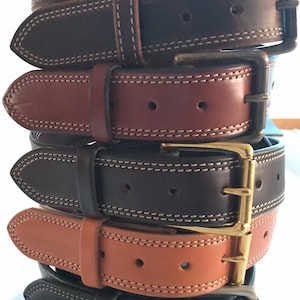 Peut inclure: Cinq ceintures en cuir de diff&eacute;rentes couleurs, empil&eacute;es les unes sur les autres. Les ceintures ont un bord &agrave; double couture et une boucle dor&eacute;e.