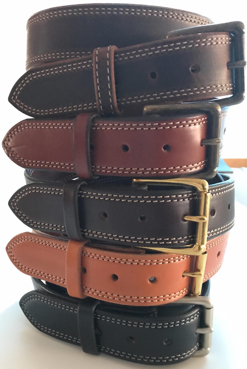 Peut inclure: Cinq ceintures en cuir de diff&eacute;rentes couleurs, empil&eacute;es les unes sur les autres. Les ceintures ont un bord &agrave; double couture et une boucle dor&eacute;e.